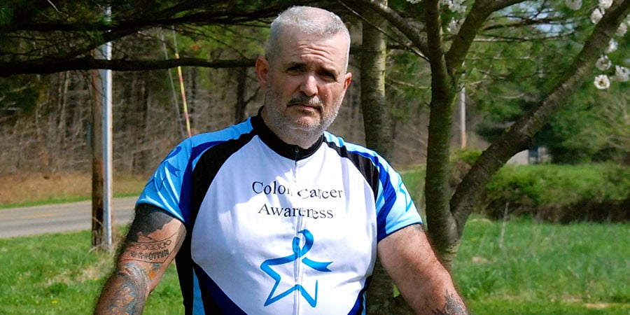 A man with tattoos standing next to a tree.