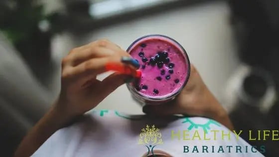 A woman drinking a smoothie with blueberries in it.