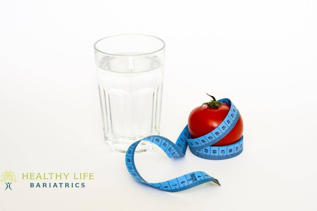 A glass of water and a tomato next to a measuring tape.