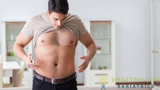 A man in a living room looking at his stomach.