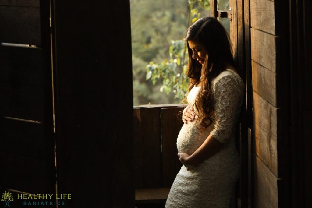 A pregnant woman in a white dress leaning against a wooden door.