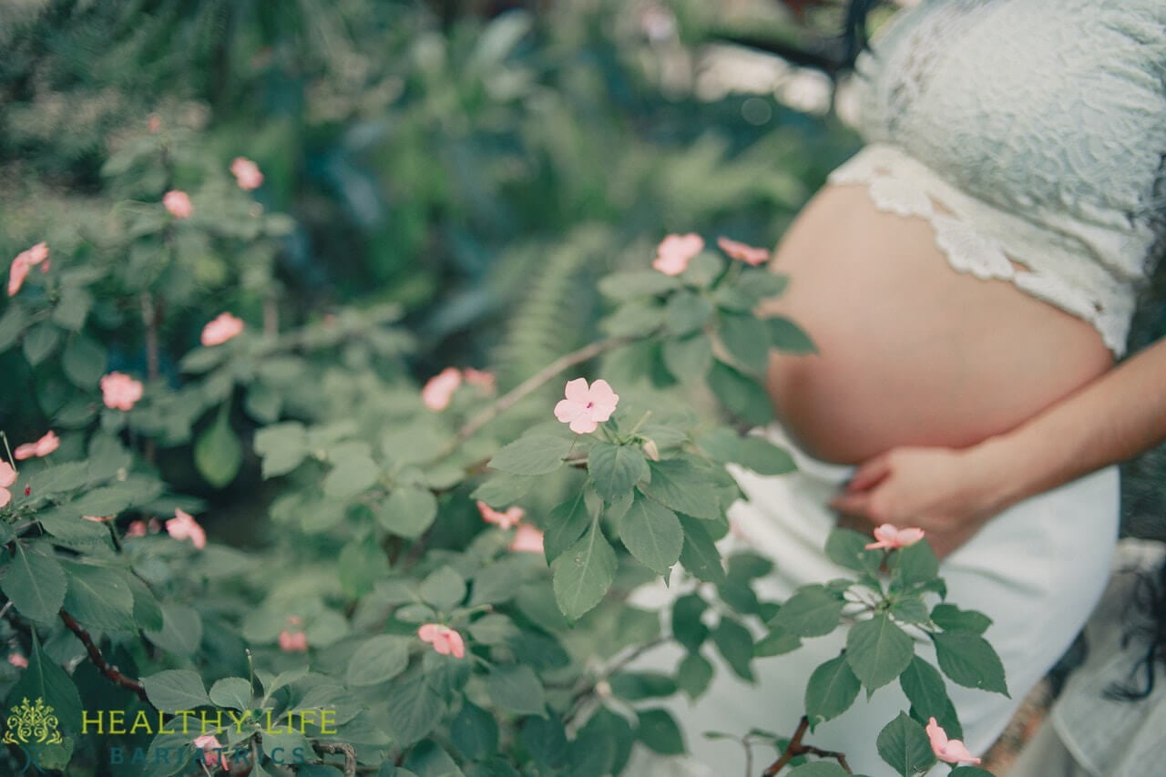 A pregnant woman standing in a garden with flowers.