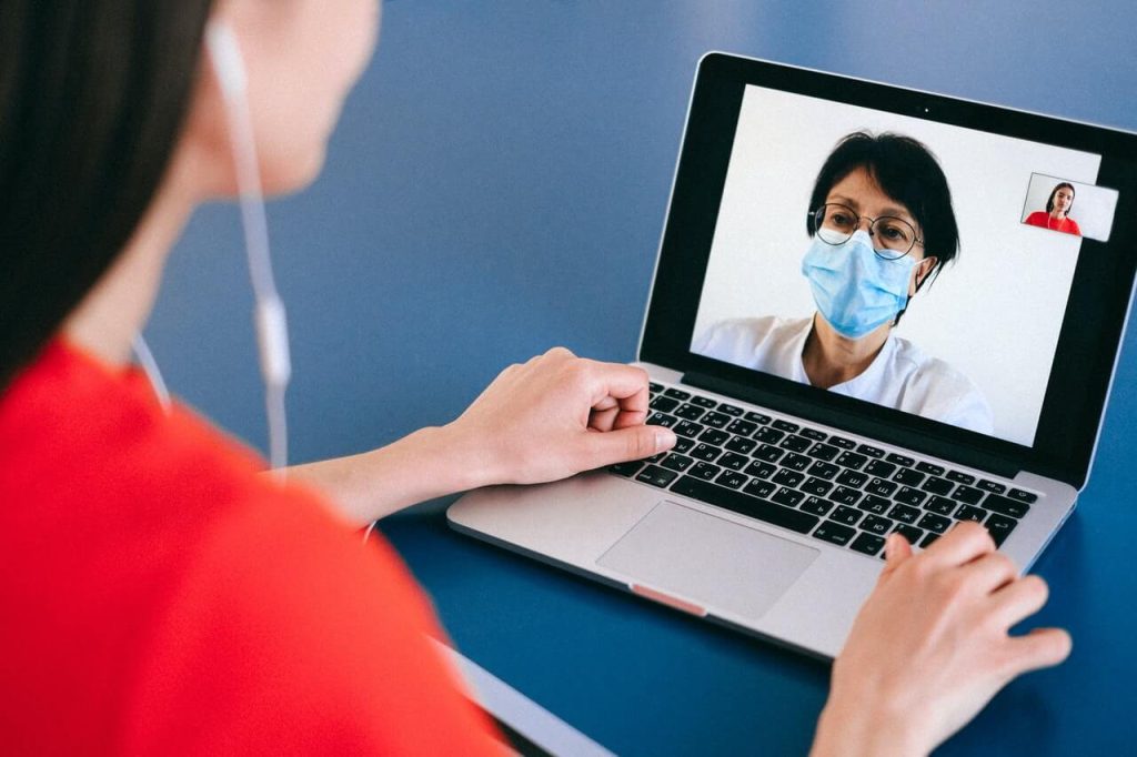 A woman wearing a surgical mask on a laptop.