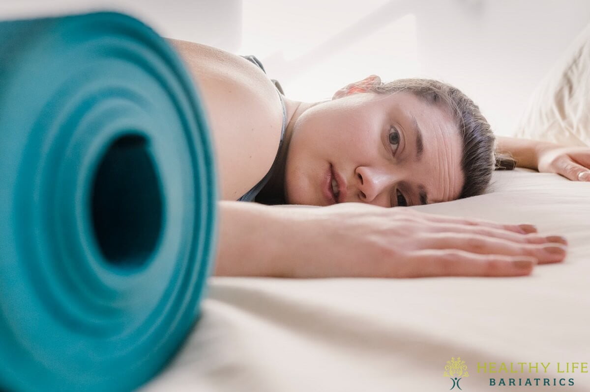 A woman laying on a bed with a yoga mat.