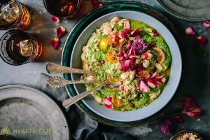 A bowl of greens and flowers on a table.