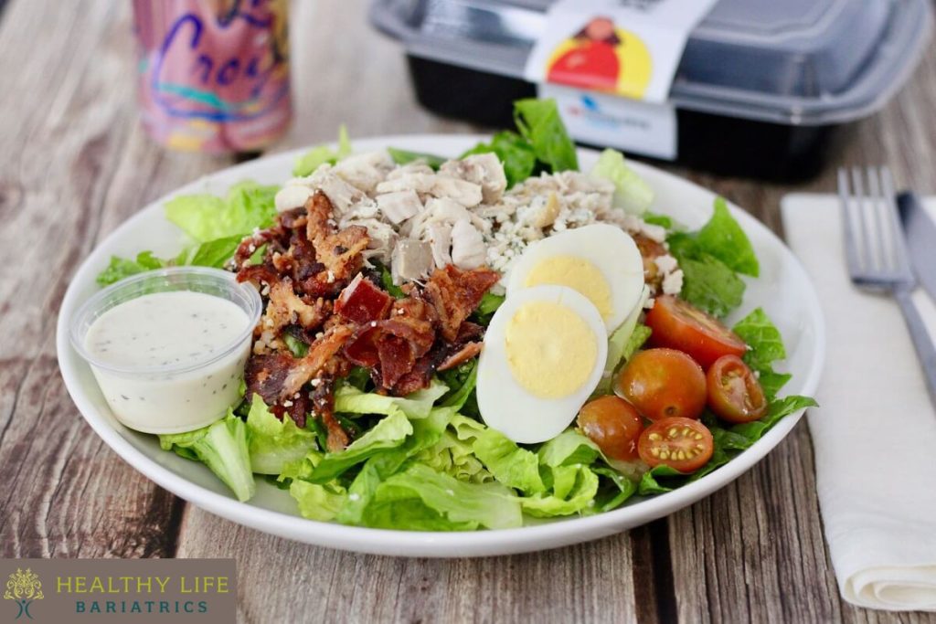 A bowl of salad with eggs, bacon, lettuce and tomatoes.