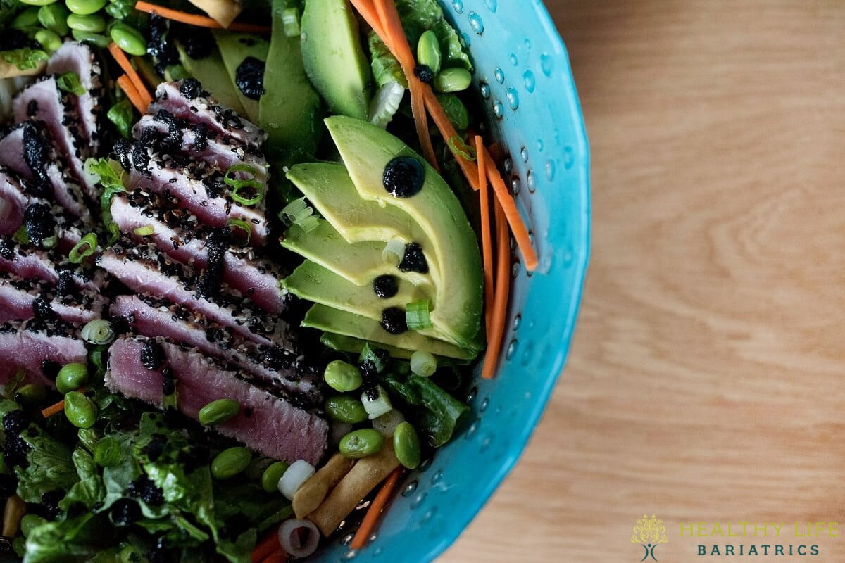 A bowl of tuna salad with avocado, peas and carrots.