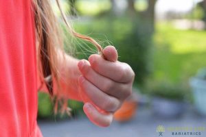 A girl's hand holding a long piece of hair.