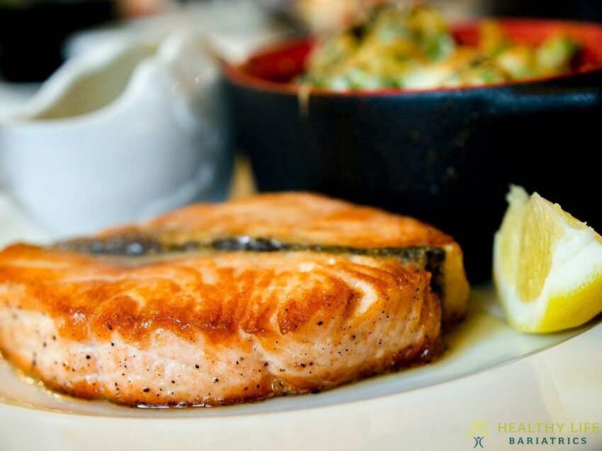 A piece of salmon on a plate with lemon wedges.