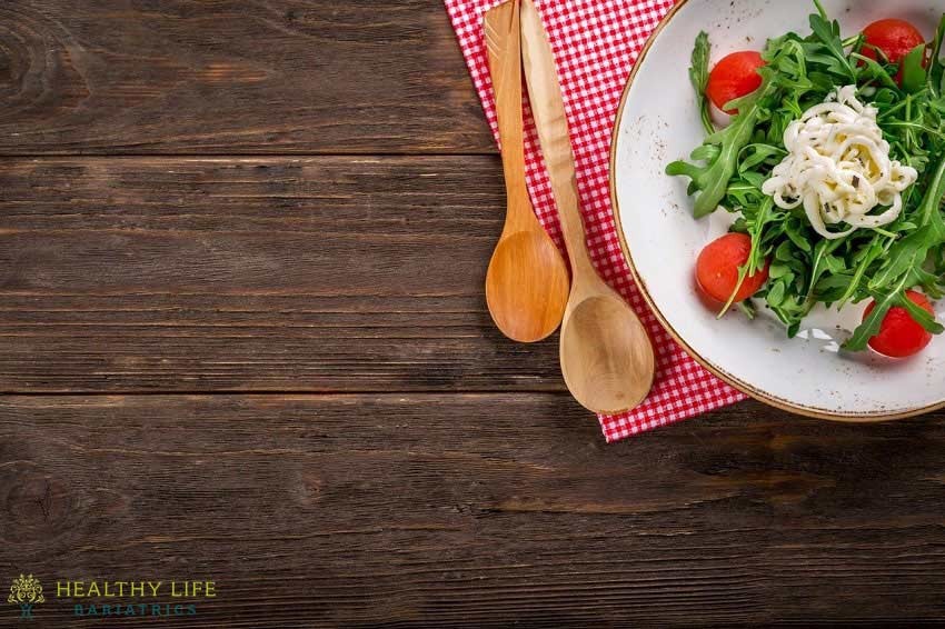 A plate of salad with tomatoes and a wooden spoon.