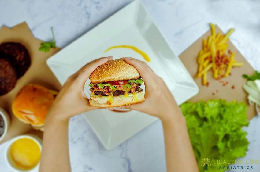 A person holding a burger with fries on a plate.