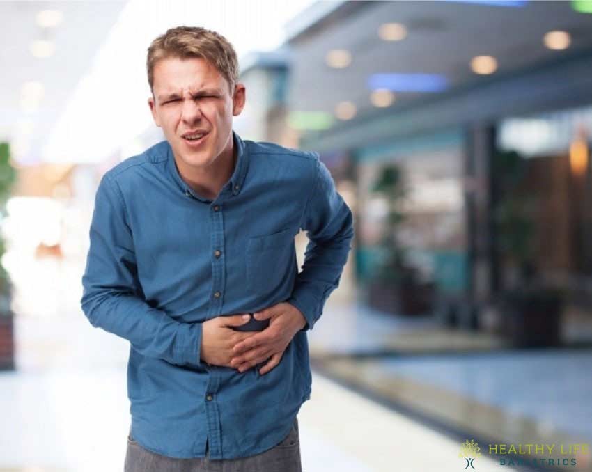 A man with a stomachache is standing in a mall.