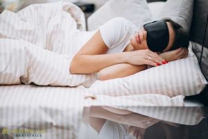 A woman sleeping in bed with a black eye mask.