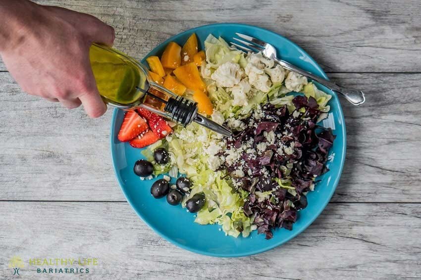 A person pouring olive oil on a plate of salad.