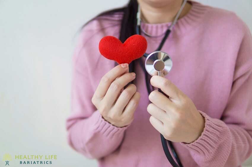 A woman holding a red heart with a stethoscope.