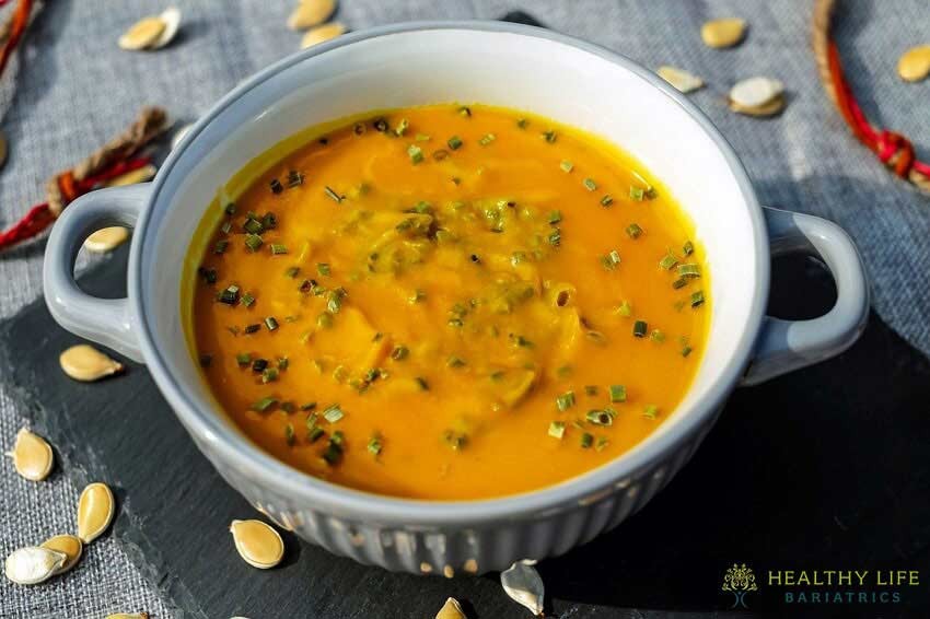 A bowl of pumpkin soup with pumpkin seeds on top.