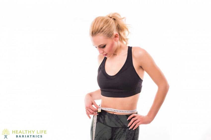 A woman is measuring her waist with a tape measure.