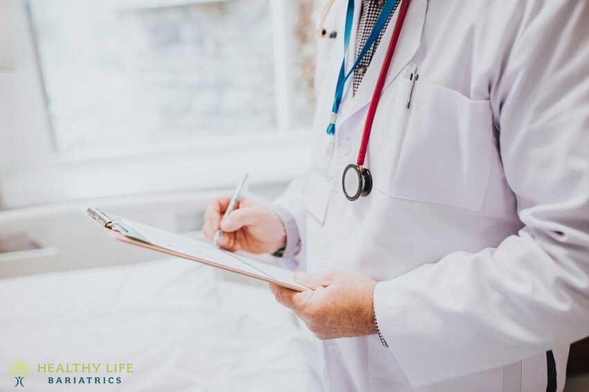 A doctor is writing on a clipboard in a hospital bed.