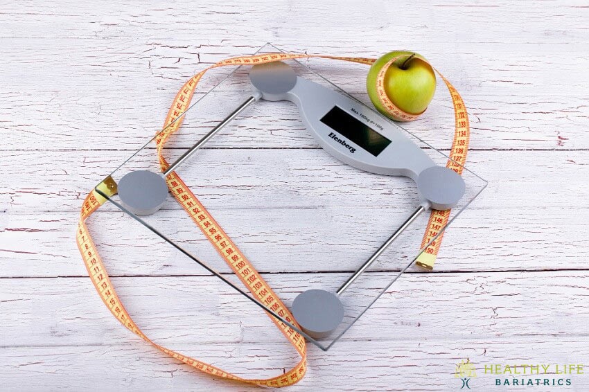 A glass scale with an apple and tape on it.