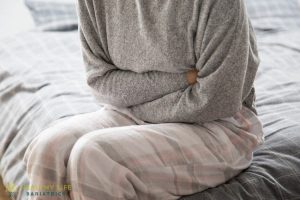 A woman sitting on a bed with her hands on her stomach.