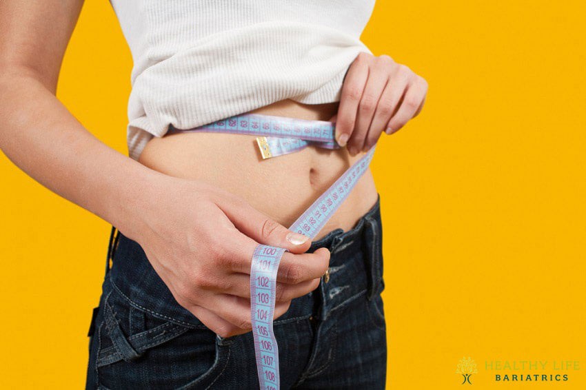 A woman is measuring her waist with a measuring tape.