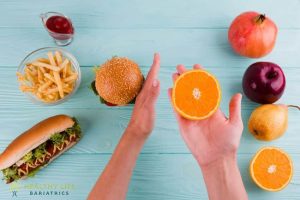 A person is holding a burger, fries and an orange.