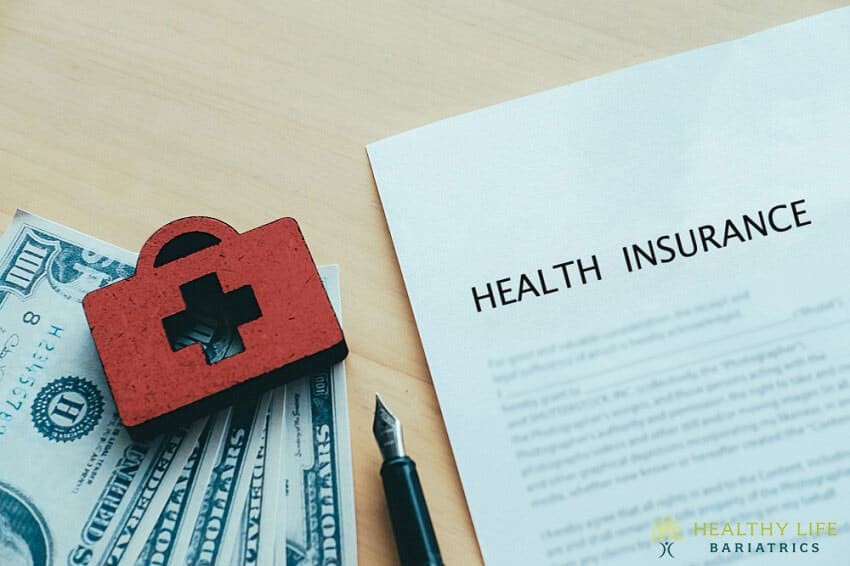 A health insurance document on a table with money and a red first aid kit.