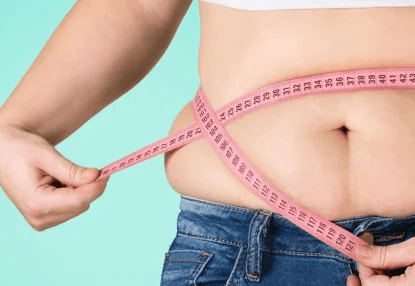 A person holding a pink measuring tape around their waist, illustrating a significant belly overhang above blue jeans against a turquoise background, possibly considering weight loss surgery in Los Angeles.